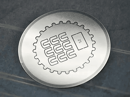 Close-up of a circular metal token with an engraved geometric design and symbols on a textured surface.